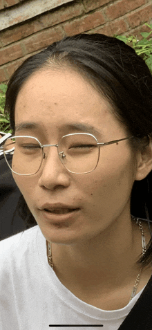 a close up of a woman wearing glasses and a white shirt with her eyes closed