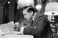 a man in a suit sits at a table reading a newspaper with the word life on the bottom right