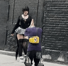 a man with a yellow bag with a skull on it is kneeling down in front of a woman in a skirt .