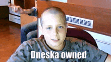 a young boy with a shaved head is sitting in front of a mirror with the words dneska owned written on it .