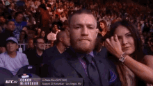 a man in a suit and tie is sitting next to a woman in a crowd at a ufc fight