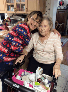 a woman wearing a sweater that says santa on it is hugging an older woman in a wheelchair