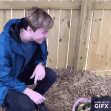 a man in a blue jacket is kneeling down next to a rabbit in a pink cage made with gifx