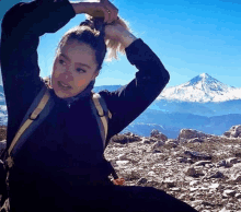 a woman with a backpack is sitting on top of a rocky hill .