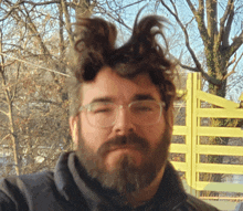 a man with glasses and a beard has his eyes closed in front of a yellow gate