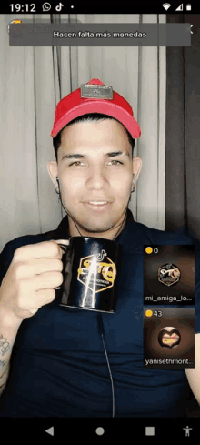 a man wearing a red hat is holding a black mug with a gold logo on it