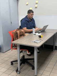 a man sits at a desk with a laptop and a bag