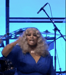 a woman in a blue dress is singing into a microphone while standing in front of a drum set .