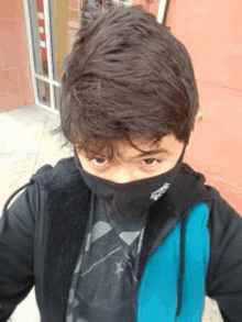 a young boy wearing a black mask and a blue vest is standing in front of a building .