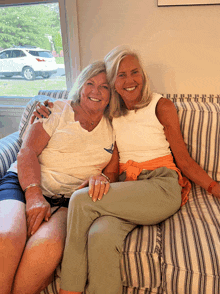 two women sit on a striped couch and smile for a picture