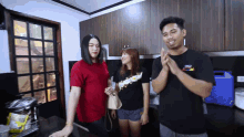 a man wearing a black shirt that says ' i love you ' on it stands in a kitchen with two other people