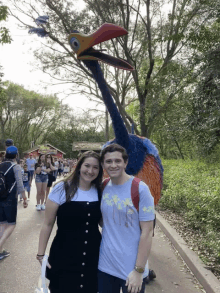 a man and a woman are posing for a picture in front of a statue of a bird