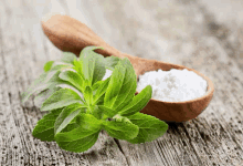 stevia leaves next to a wooden spoon filled with stevia powder