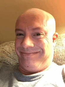 a man with a shaved head is smiling while sitting on a couch