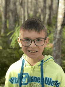 a young boy wearing glasses and a green disney world sweatshirt