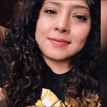 a woman with curly hair is smiling and wearing a black shirt with a gold star on it