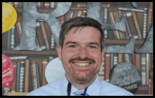 a man with a beard is smiling in front of a bookshelf