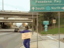 a man holding a sign that says " i 'll pay no fine " stands in front of a highway sign