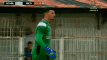 a soccer player in a green jersey stands in front of a fence during a match between usma and mco