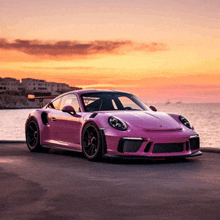 a pink porsche is parked on the side of the road at sunset