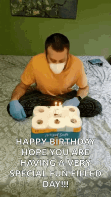 a man wearing a mask is sitting on a bed with a birthday cake made out of toilet paper rolls