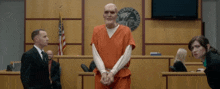 a man in handcuffs stands in a courtroom with a county seal on the wall behind him