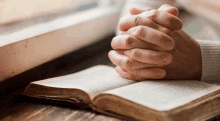 a person is praying with their hands folded over a bible