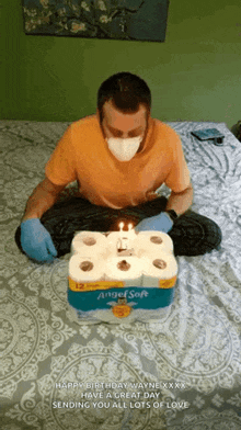 a man wearing a mask and gloves is sitting on a bed with a birthday cake made out of toilet paper rolls