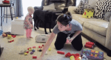 a woman is kneeling on the floor in a living room with toys and a baby and a dog .