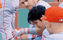 a group of baseball players are sitting in the dugout and one of them is wearing a red hat .