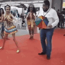 a man in a white shirt is holding a colorful umbrella in front of a group of dancers on a red carpet