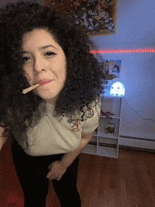 a woman with curly hair is smoking a cigarette and wearing a shirt that says atari