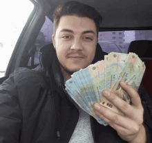 a man in a car holds up a stack of money with the number 20 on it