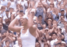 a woman in a white nike tank top is holding a tennis racquet in front of a crowd of people