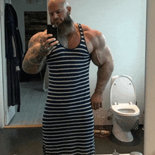 a muscular man in a striped dress is taking a selfie in front of a toilet .