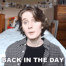 a young man is standing in front of a bed with the words back in the day written on his shirt