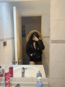 a woman taking a selfie in front of a mirror with a bottle of fixing spray on the counter