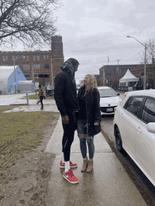 a man and a woman are standing on a sidewalk with a white car parked behind them