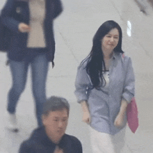 a woman in a blue shirt is walking down a hallway next to a man in a black shirt