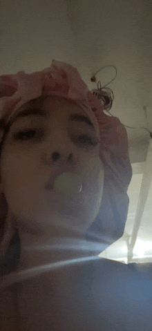 a woman wearing a pink shower cap is blowing bubbles in her mouth .