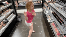 a little girl in a pink shirt is standing in front of a display of lipsticks