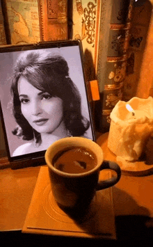 a cup of coffee next to a picture of a woman and a candle