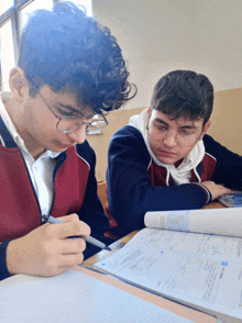 two boys are sitting at a desk with a book open to a page that says " algebra "