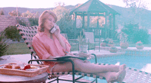 a woman in a pink shirt is talking on a cell phone by a pool