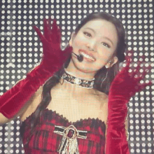 a woman wearing red gloves and a choker is standing in front of a polka dot wall .