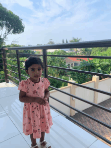 a little girl in a pink dress with butterflies on it stands on a balcony