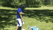 a woman in a blue shirt and white shorts is standing in a grassy field holding a golf club .