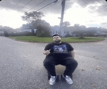 a man wearing a black shirt with a picture of a man on it sits on the side of the road