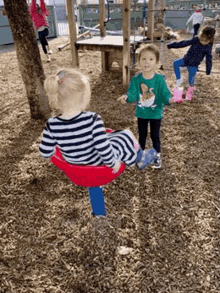 two little girls are playing on a playground . one of the girls is sitting on a red swing .