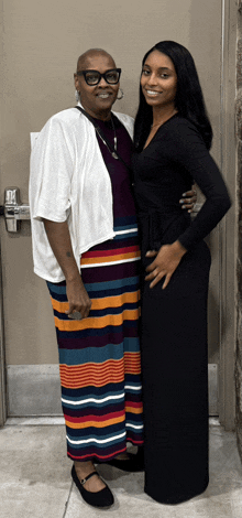 a woman in a striped skirt stands next to a woman in a black dress